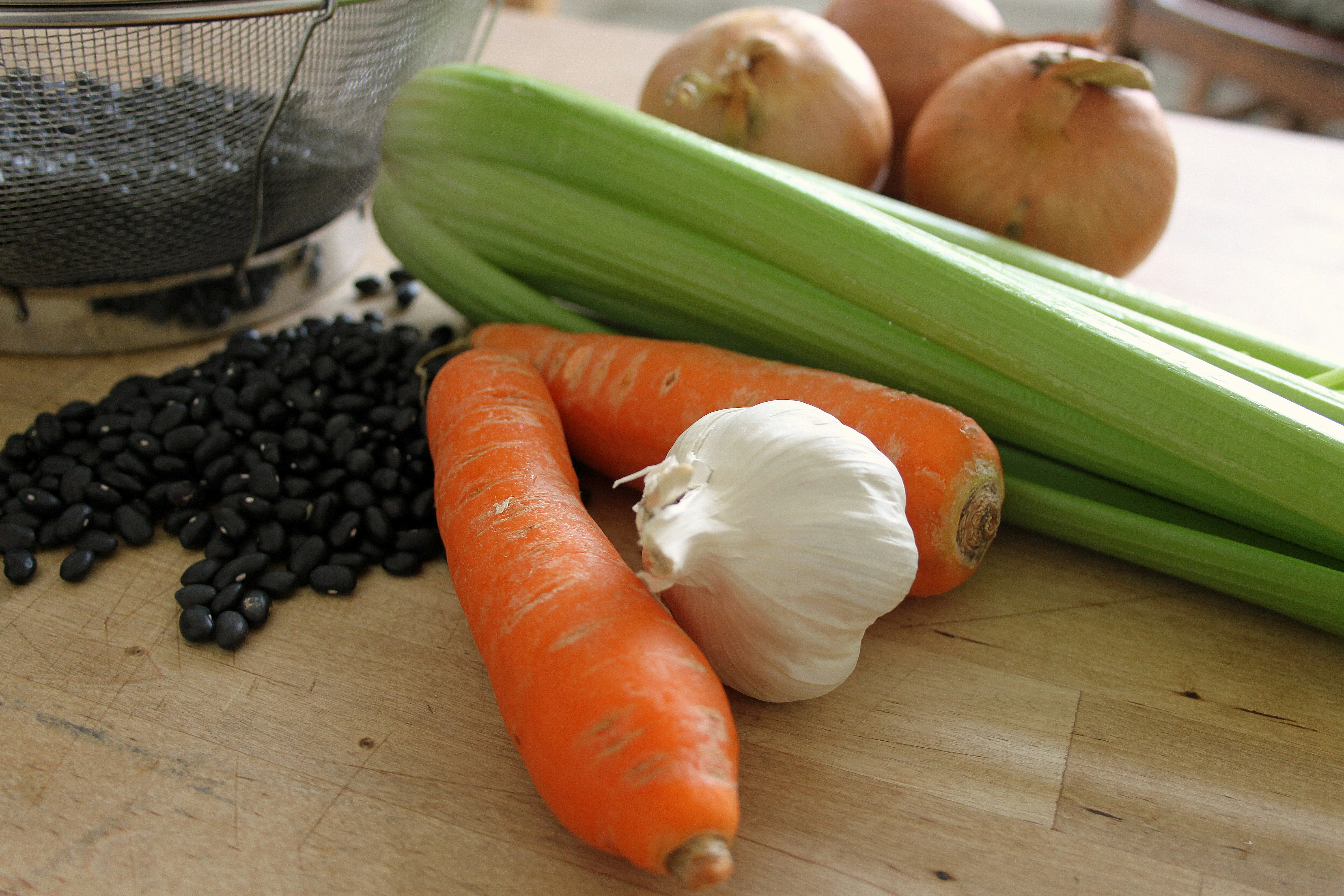 Carrots, celery, onions, garlic and black beans arranged on a wooden chopping surface.