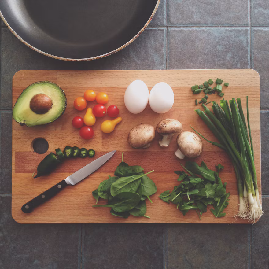 Avocado, tomatoes, eggs, mushrooms and greens on a cutting board.