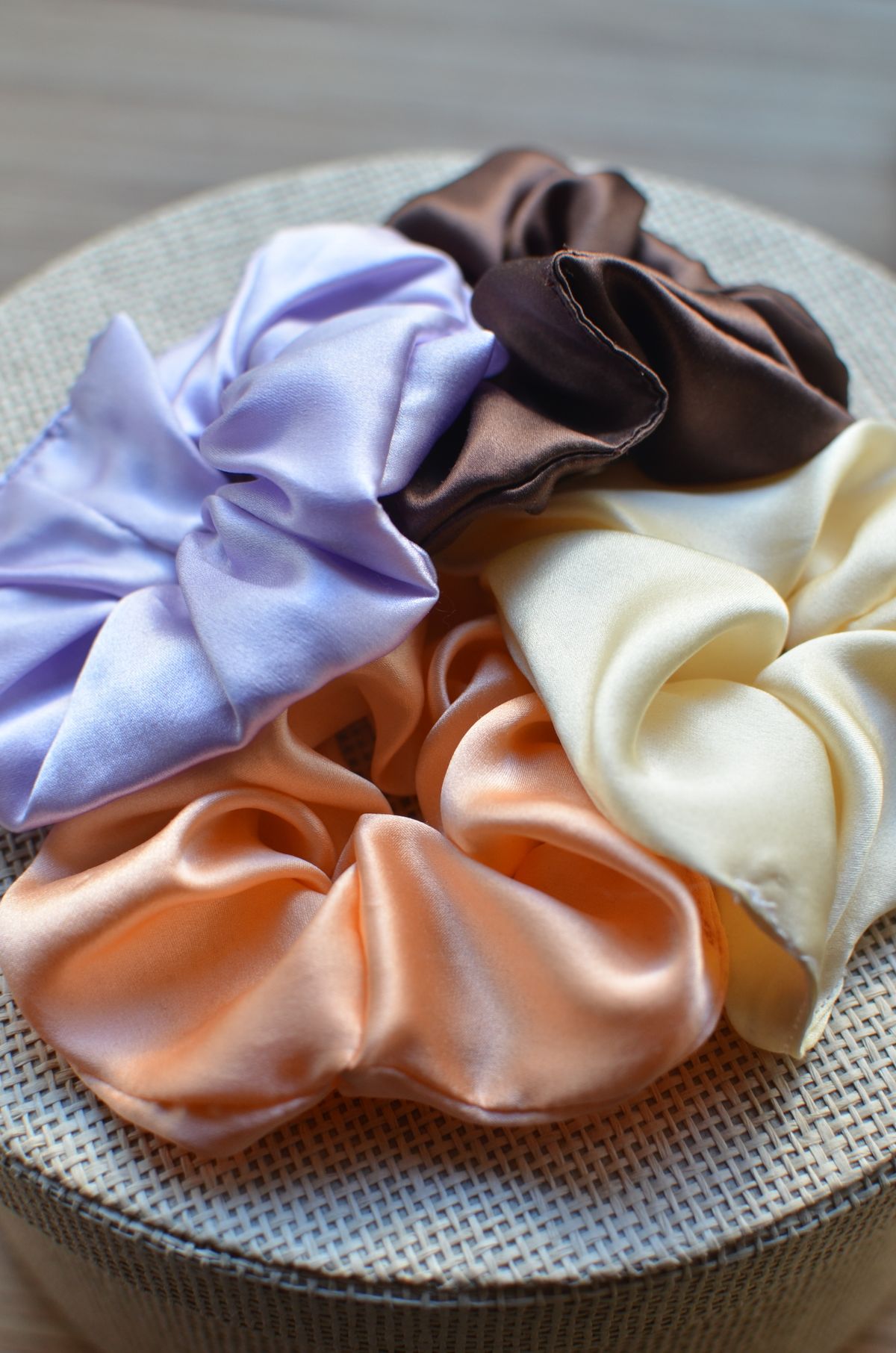 Peach, cream, brown and lavender scrunchies lie on a round woven box.