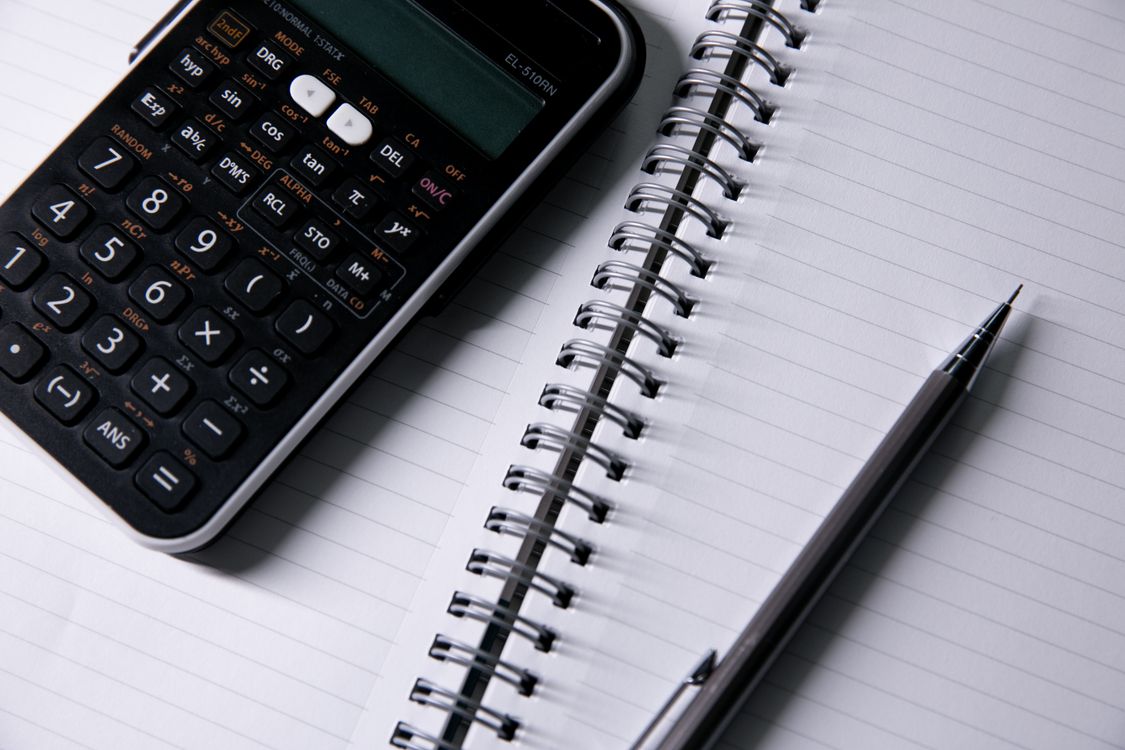 An open lined notebook lies beside a calculator and pen.
