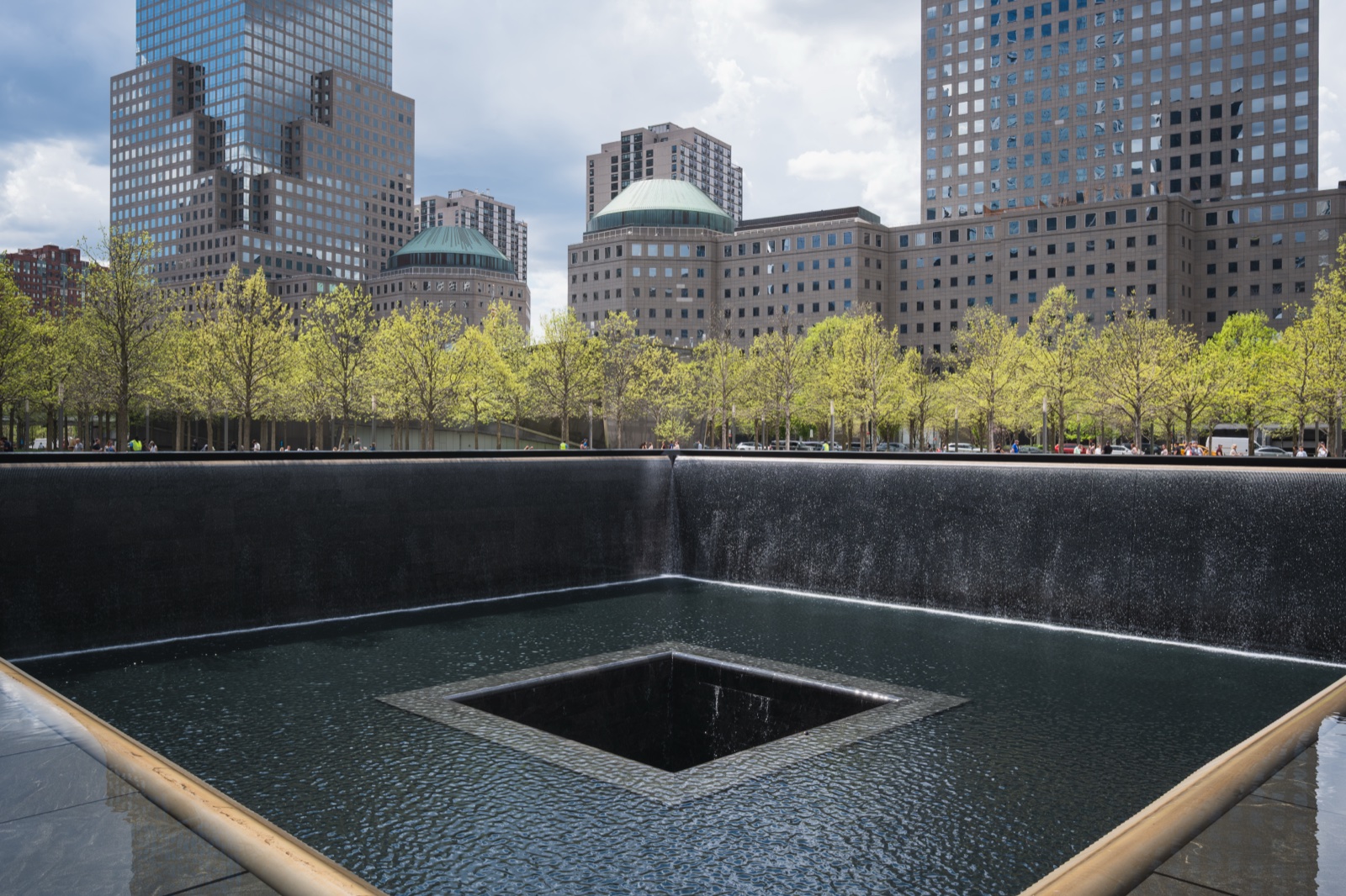 The north reflecting pool at the National September 11 Memorial, with trees and buildings beyond it.