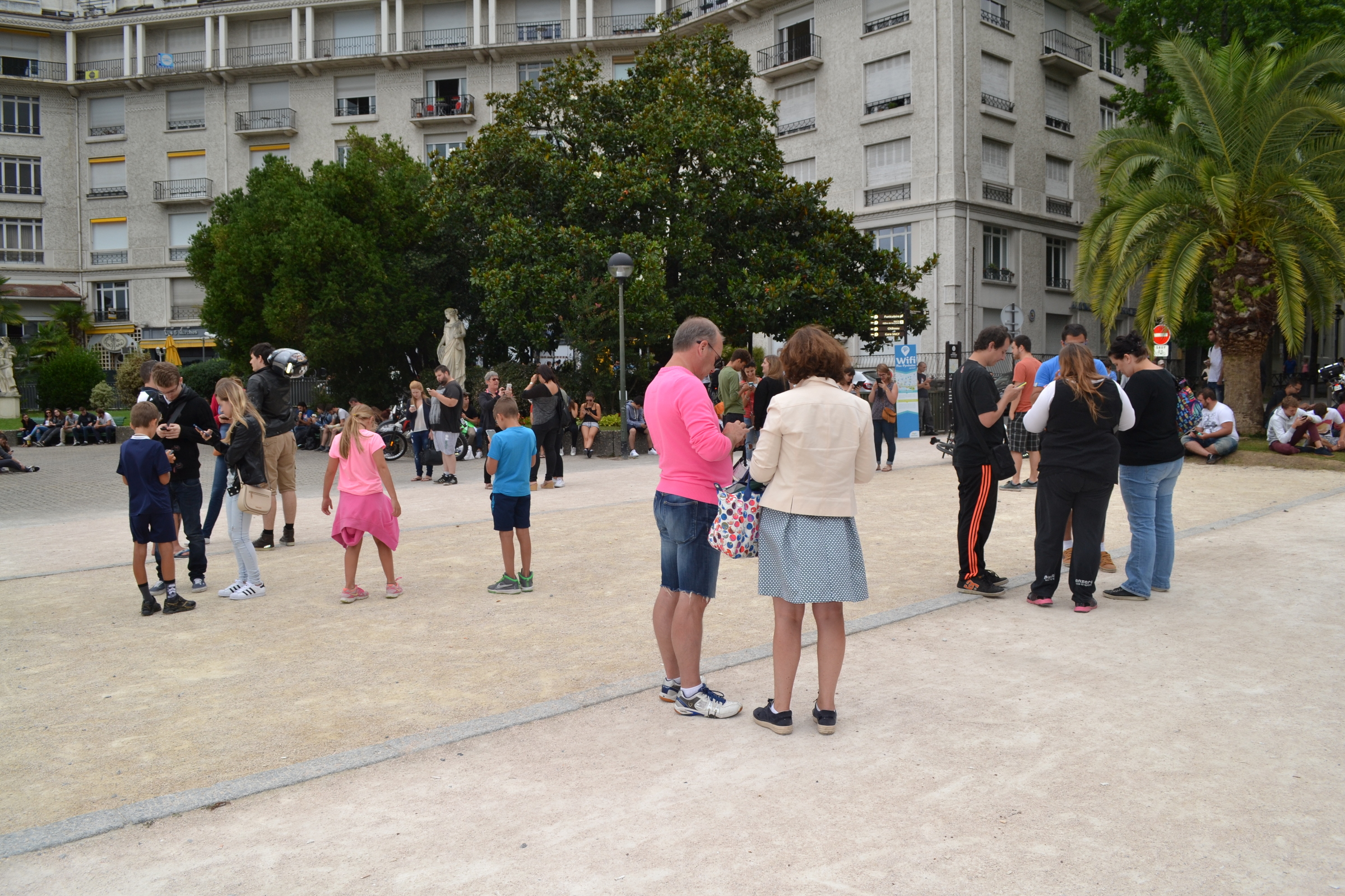 Groups of people look at their phones in an outdoor square in Pau.