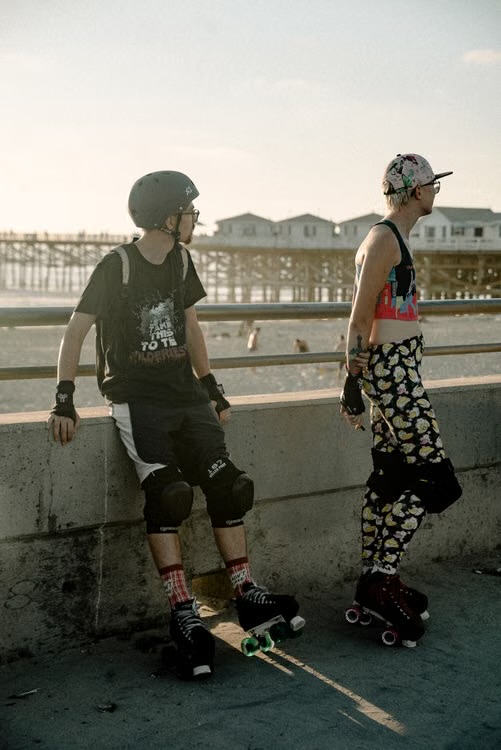 Two people wearing roller skates pause beside a waterfront railing.
