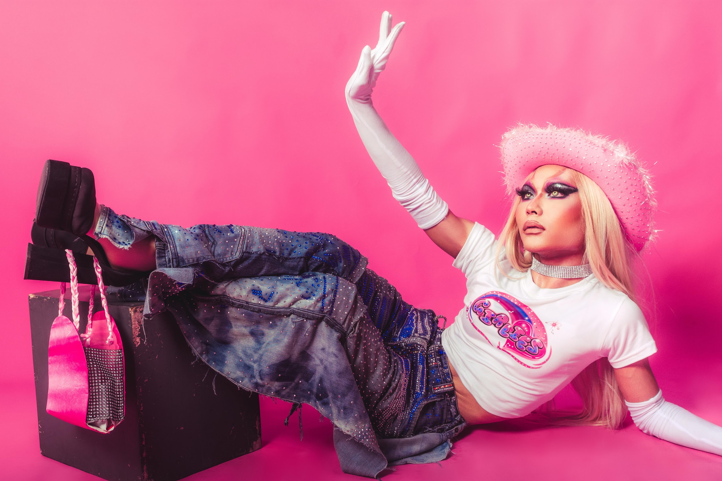 A person in a pink cowboy hat and white gloves poses in embellished denim with platform boots and a pink bag.