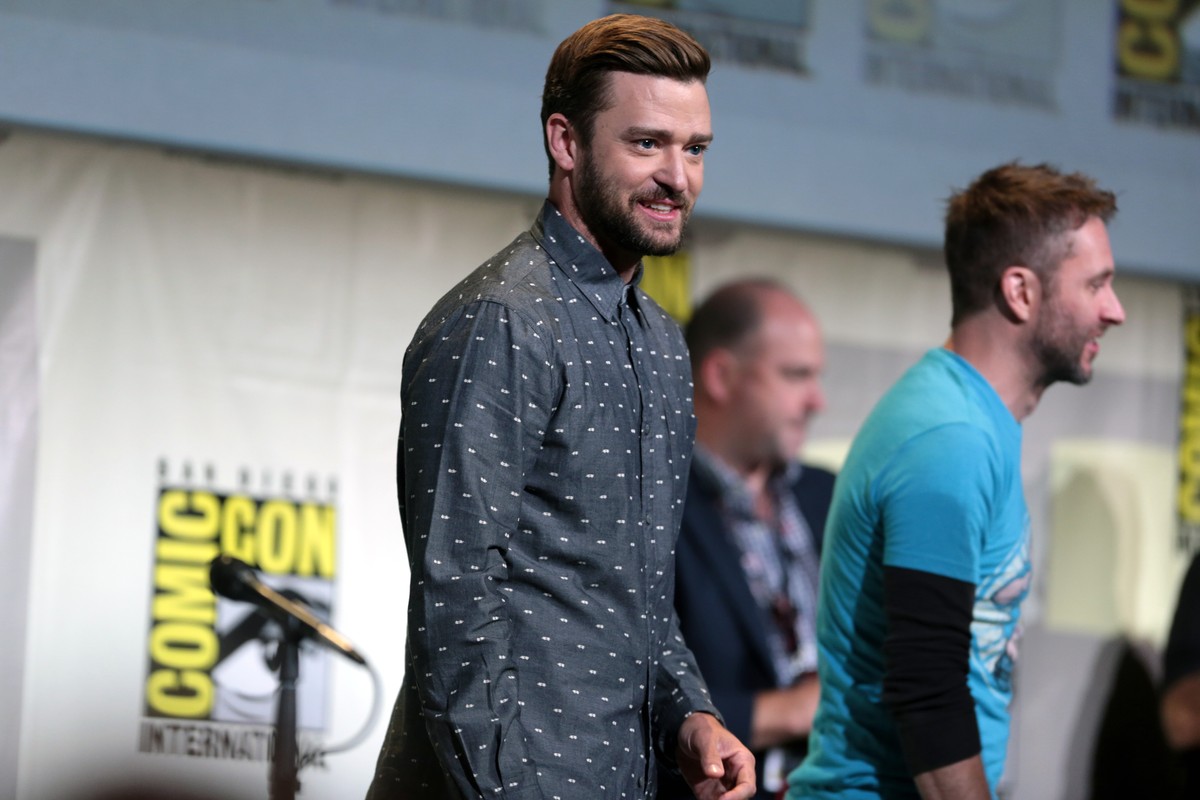 Justin Timberlake in a patterned shirt at a public event, with other people behind him.