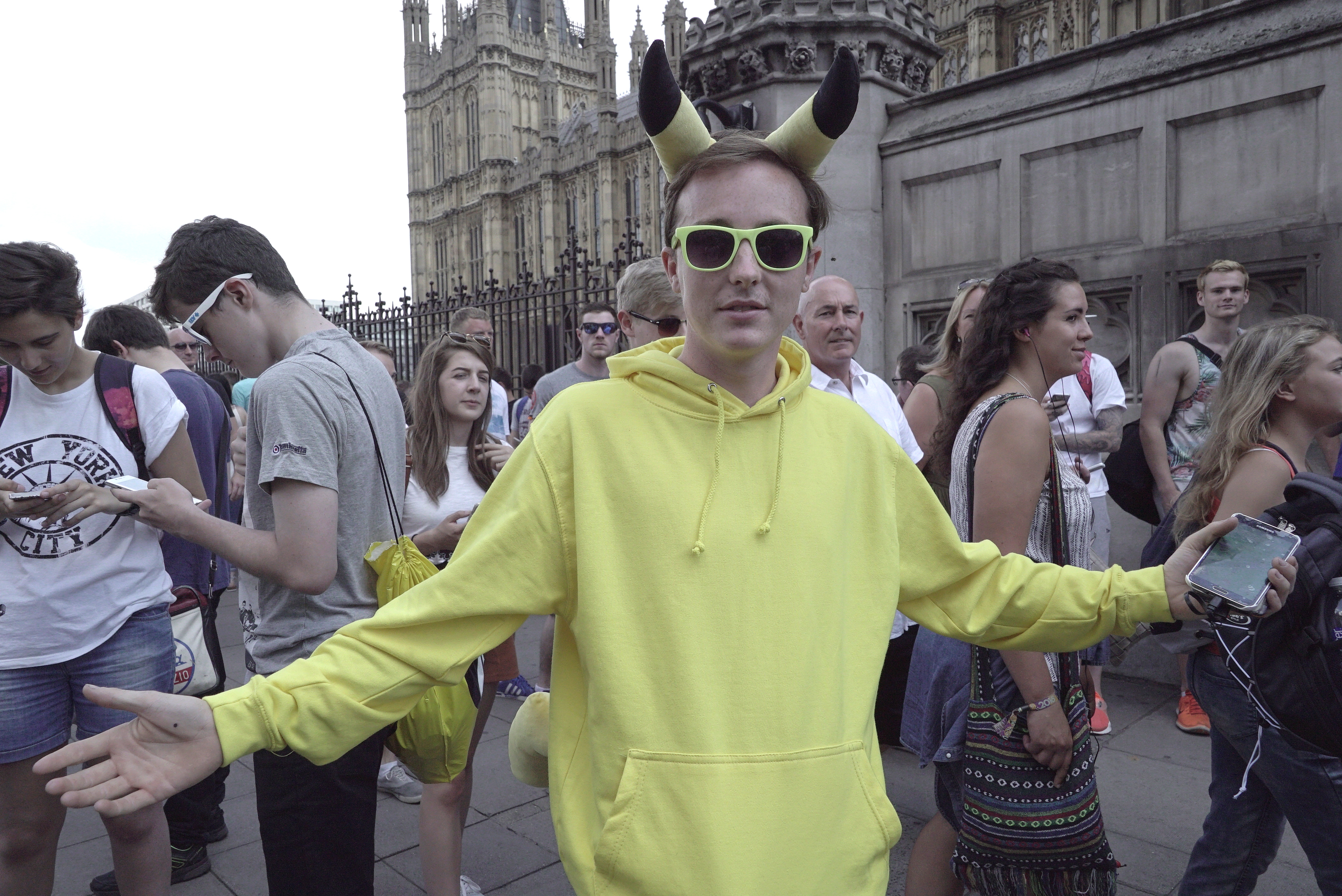 A participant wearing Pikachu ears stands among people holding phones at a London Pokémon GO gathering.