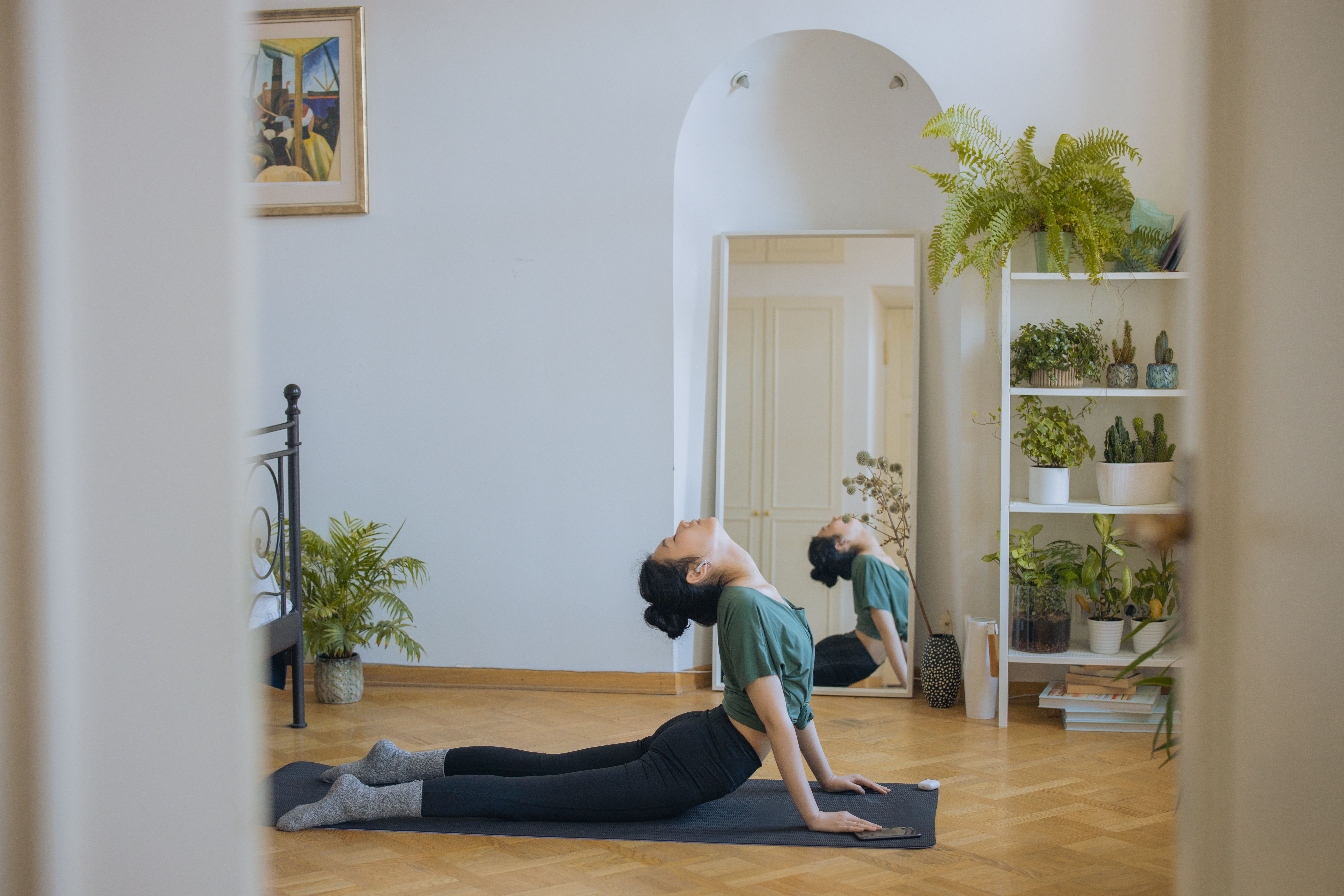 A woman raises her chest from an exercise mat in a room with a mirror and houseplants.