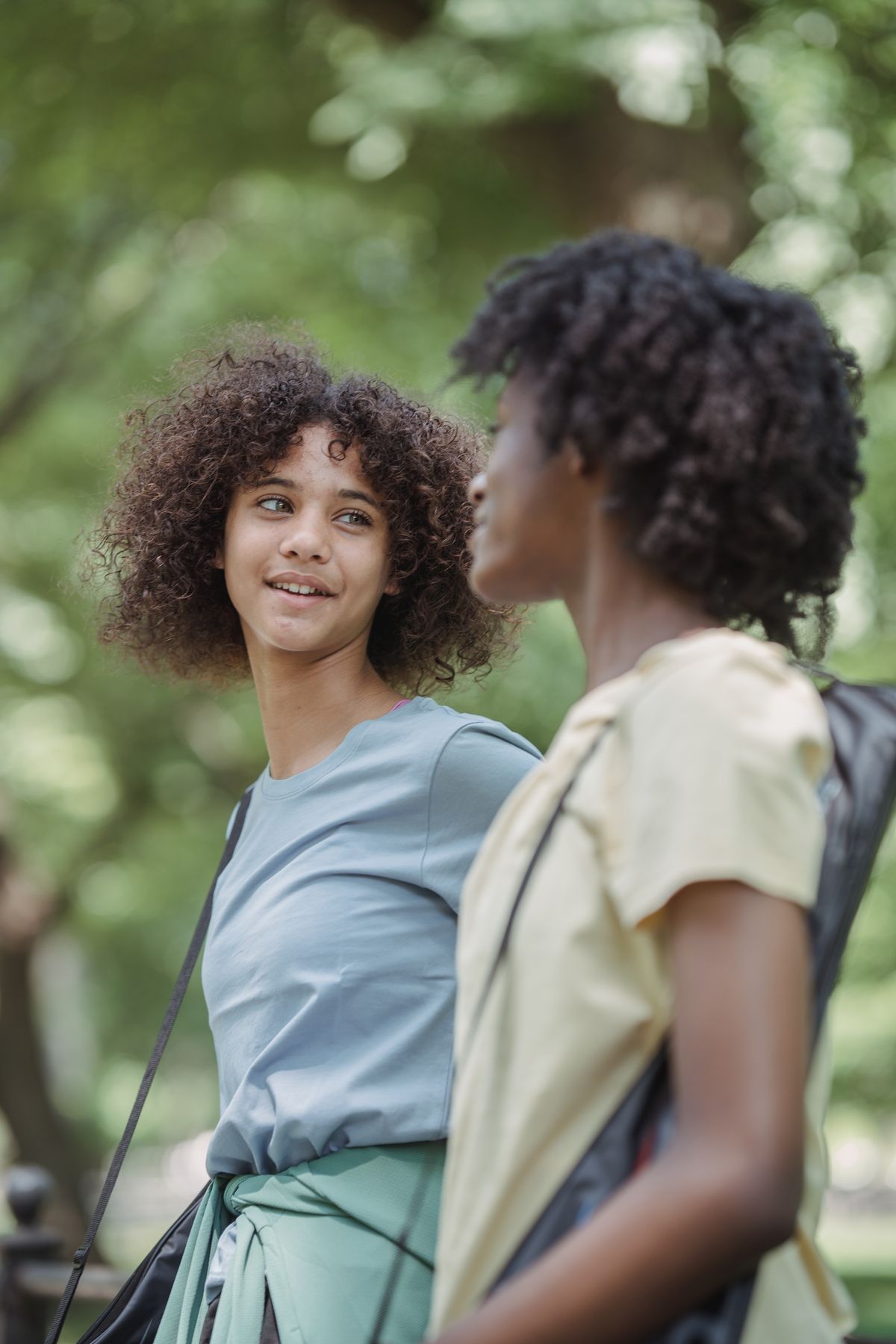 Two people talk outdoors beside green trees.